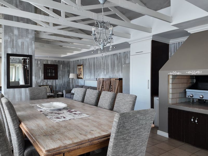 Spacious open-plan living and dining area featuring exposed timber ceiling beams, a built-in indoor braai, and neutral tiled flooring.