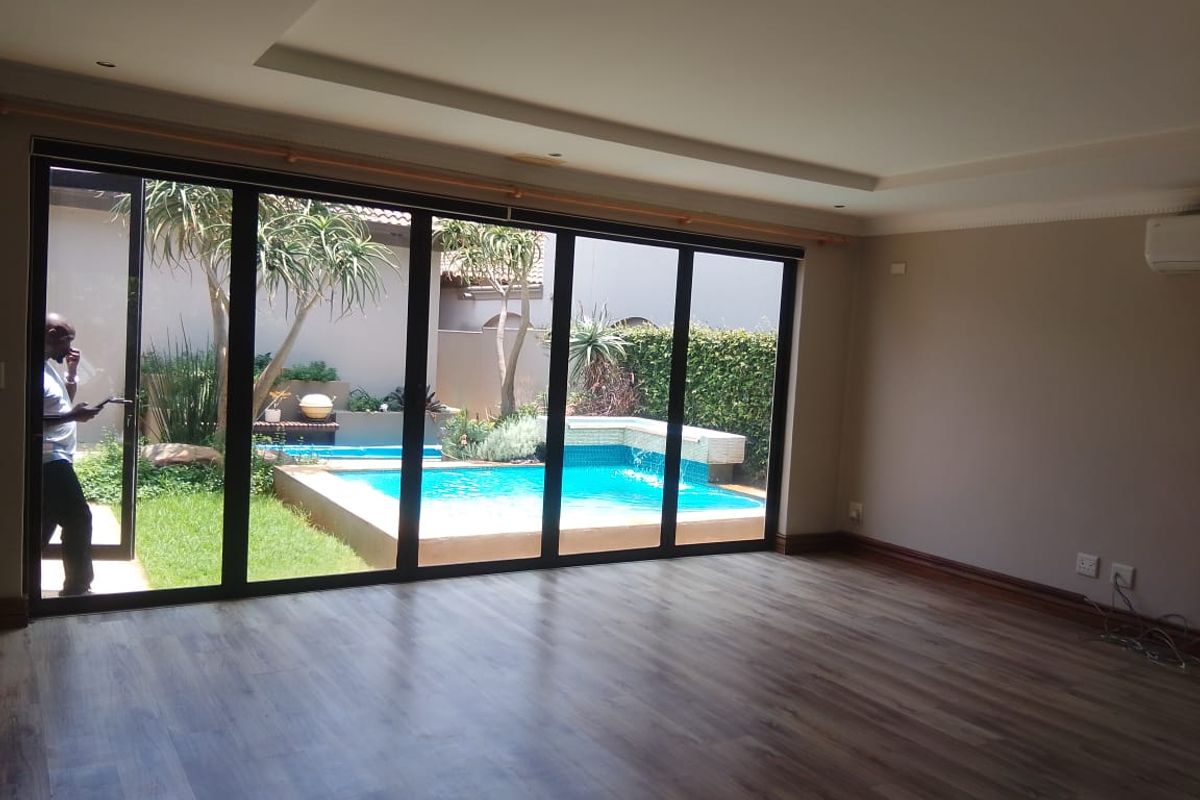 Spacious living area featuring modern laminate flooring, recessed ceiling, and large stacking glass doors opening onto a private garden and swimming pool.