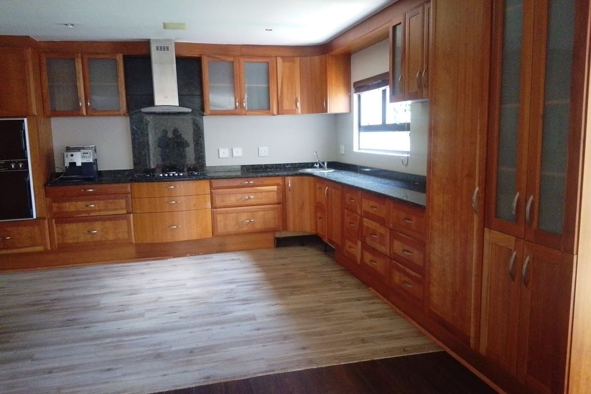 A spacious kitchen featuring extensive wooden cabinetry, granite countertops, built-in oven, and a stainless steel extractor fan, offering a functional layout.