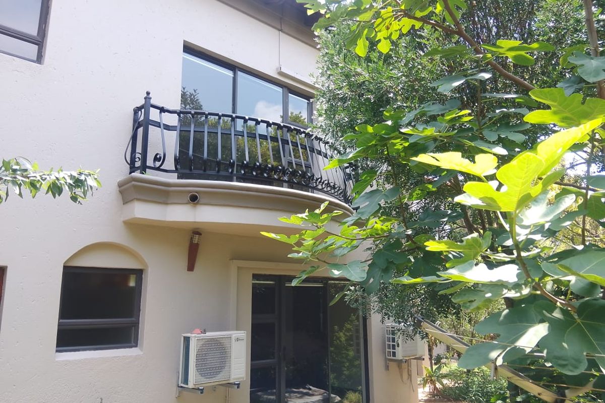 Rear view of the property featuring a curved balcony with wrought iron railing, sliding glass doors, and external air conditioning units.