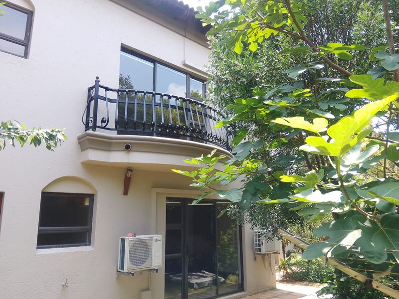 Rear view of the property featuring a curved balcony with wrought iron railing, sliding glass doors, and external air conditioning units.
