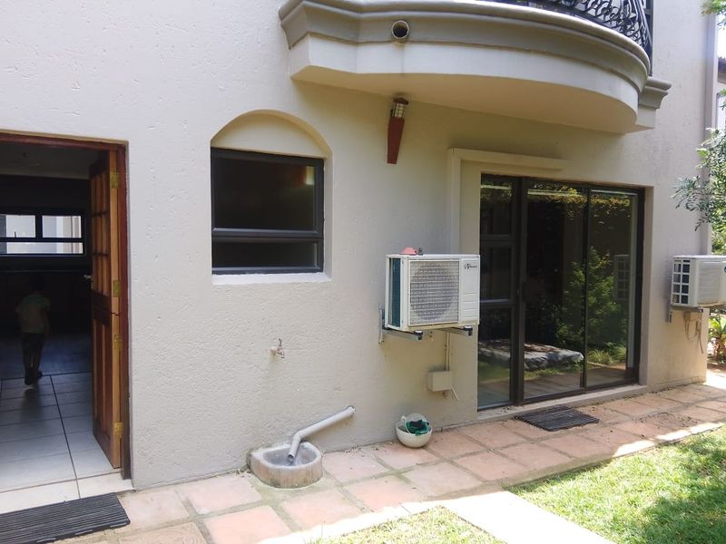 Rear exterior view showing a tiled patio, sliding glass doors, air conditioning units, and access to the interior living space.