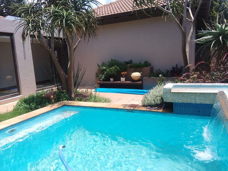 A well-maintained outdoor pool area featuring a built-in water feature, tiled coping, and integrated garden planter boxes.