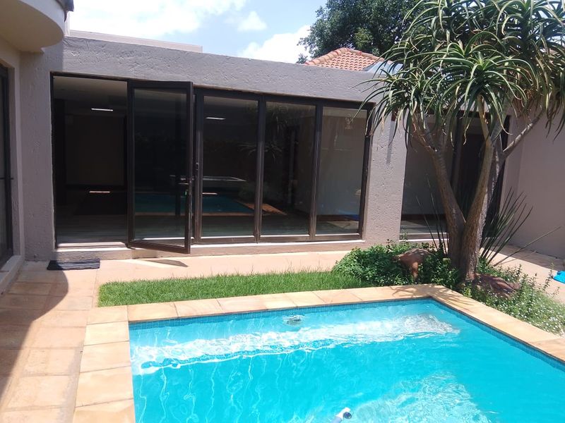 A well-maintained outdoor pool area featuring stone coping, a paved patio, and large sliding glass doors providing seamless access to the interior living space.
