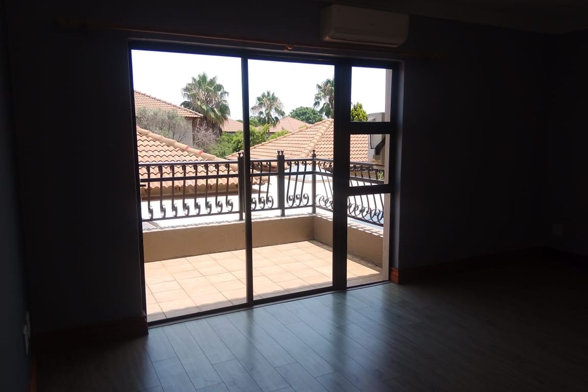 An empty bedroom featuring laminate flooring, a wall-mounted air conditioning unit, and a sliding glass door leading to a private balcony with iron railings.