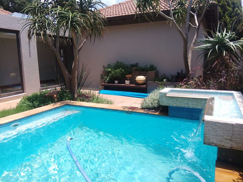 A well-maintained outdoor pool area featuring a built-in water feature, tiled surround, and integrated planter boxes, set against a private garden backdrop.
