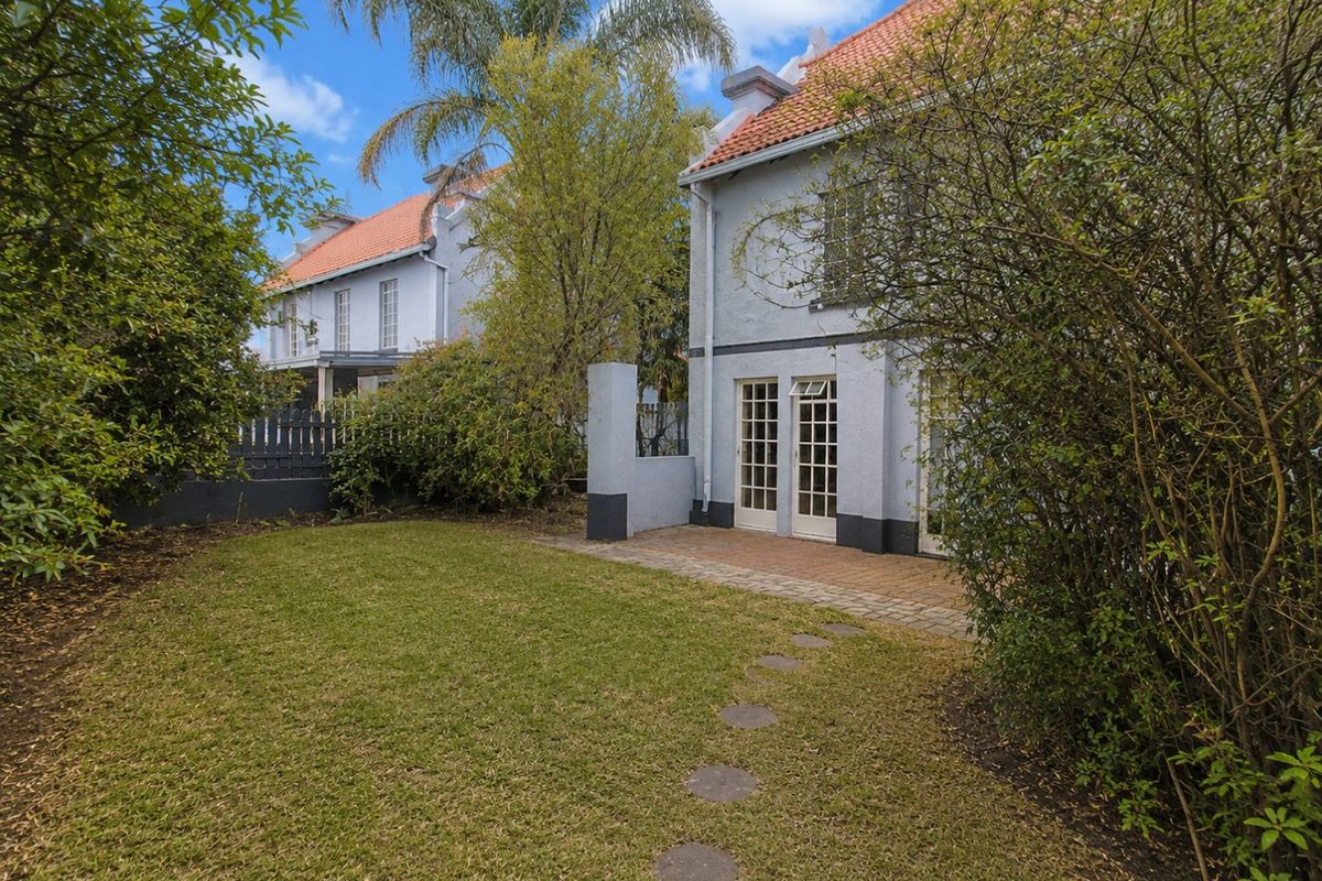 Rear view of the townhouse featuring a paved patio area, established garden, and classic french doors leading into the residence.