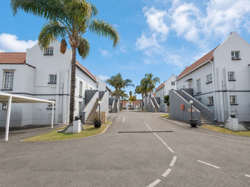 A view of the townhouse complex driveway featuring paved access, external staircases, and covered parking structures within a well-maintained residential estate.