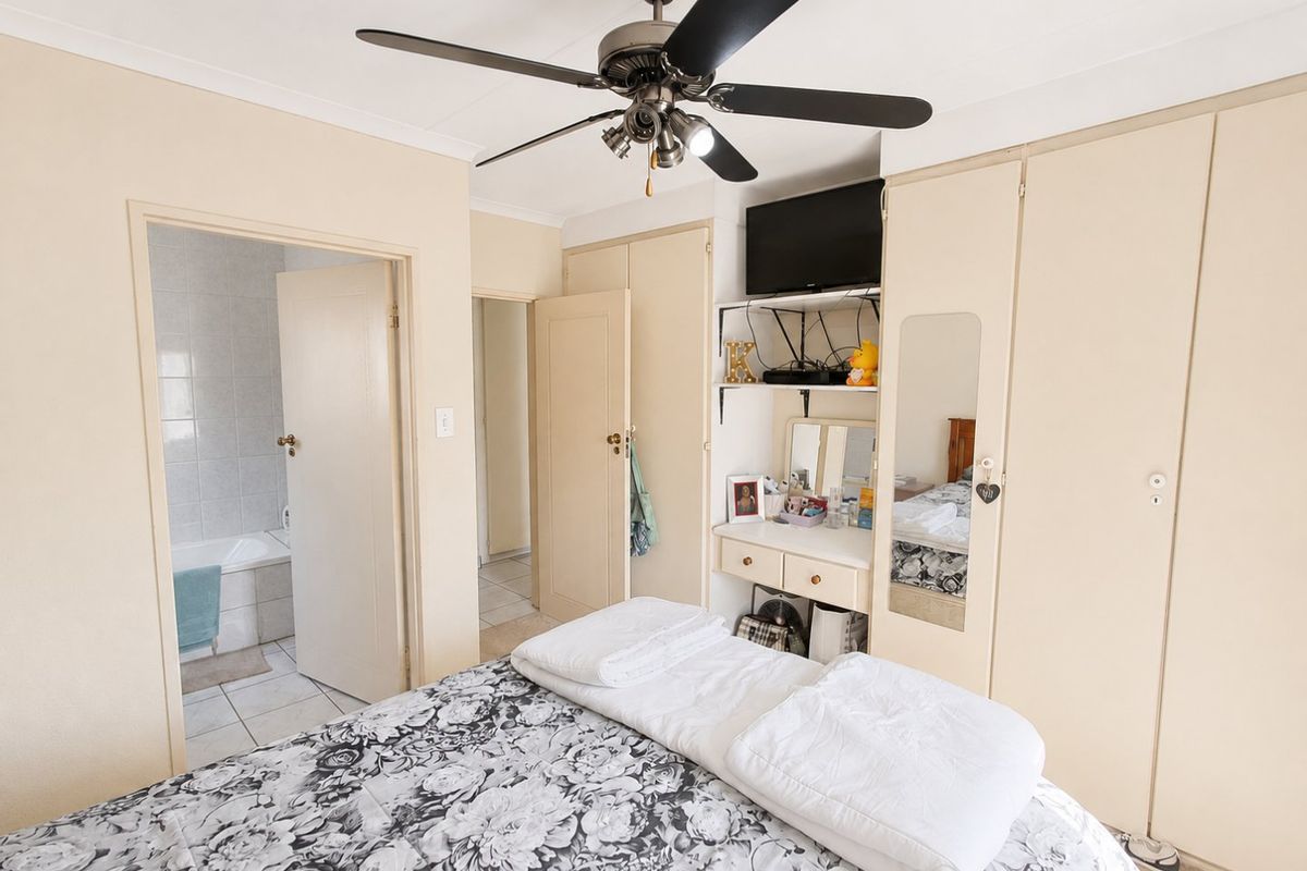 A bedroom featuring built-in cupboards, a ceiling fan, and direct access to an en-suite bathroom with tiled flooring.