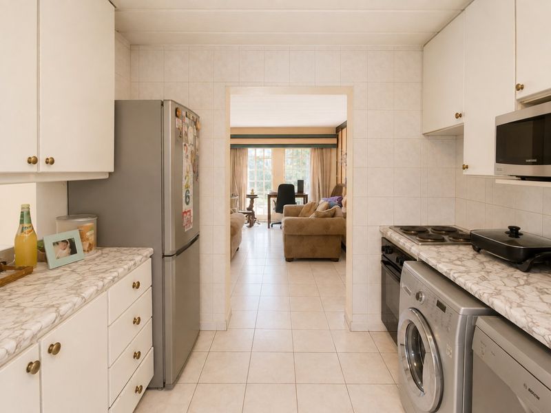 A functional kitchen featuring white cabinetry, laminate countertops, and tiled finishes, with a direct view into the adjacent living area.
