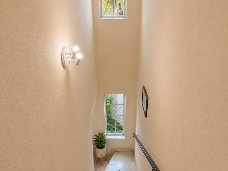 A bright and well-maintained staircase featuring tiled steps, a sturdy handrail, and tall windows that provide natural light to the hallway.