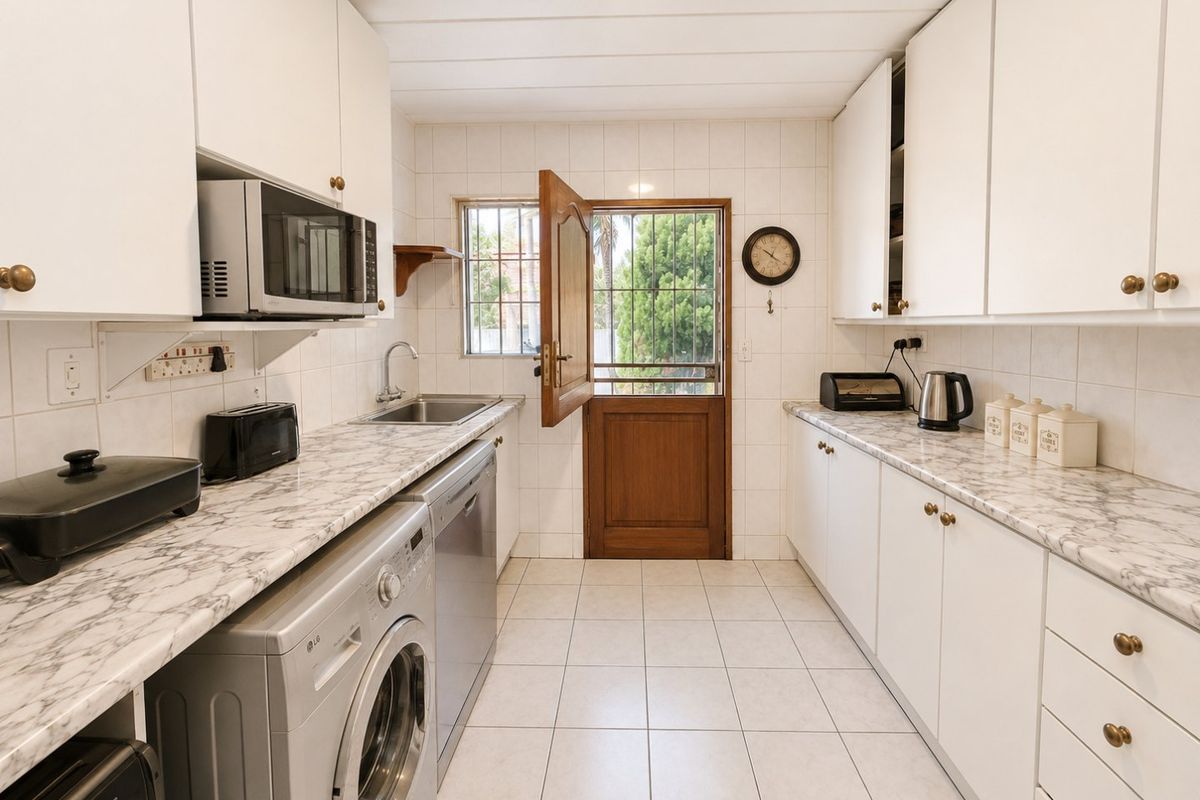 A functional kitchen featuring white cabinetry, marble-effect countertops, tiled flooring, and direct access to the exterior via a secure timber door.