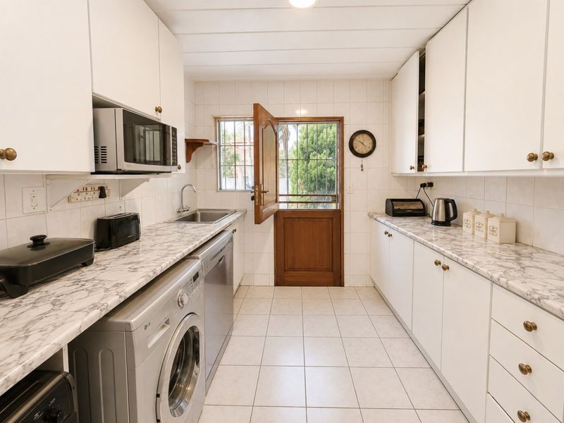 A functional kitchen featuring white cabinetry, marble-effect countertops, tiled flooring, and direct access to the exterior via a secure timber door.