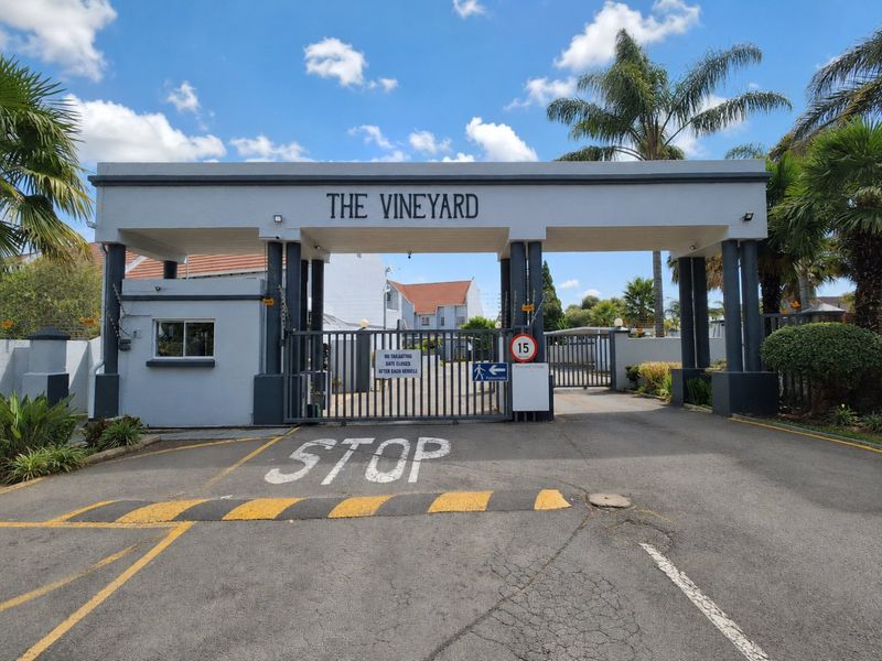 The main entrance gate to The Vineyard complex, featuring a secure access point, guard house, and paved driveway with speed bump.