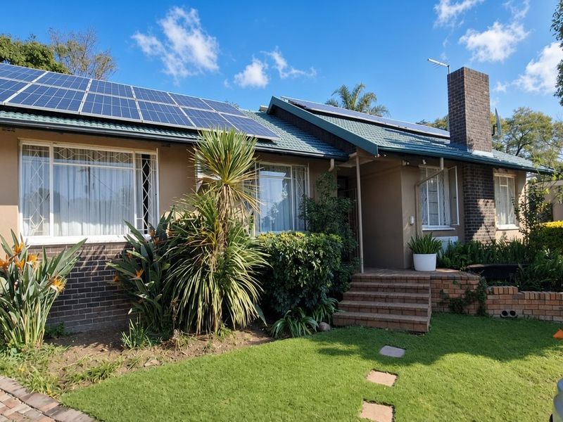 Front elevation of a single-story house featuring a tiled roof with integrated solar panels, brick chimney, and landscaped front garden with brick steps.