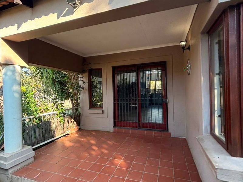 A covered patio area featuring tiled flooring, a sliding door with security gate, and a structural support column.