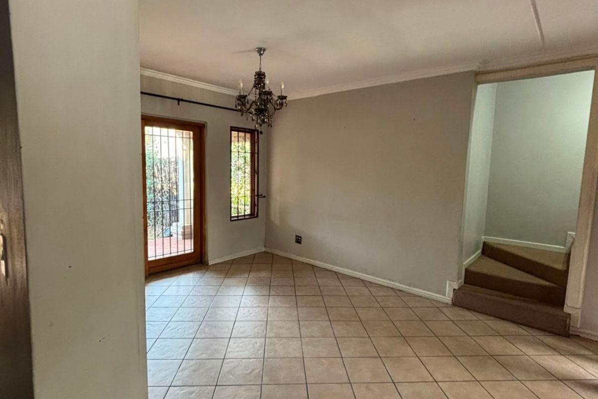 An empty living room featuring tiled flooring, a staircase, and a security gate leading to the exterior.