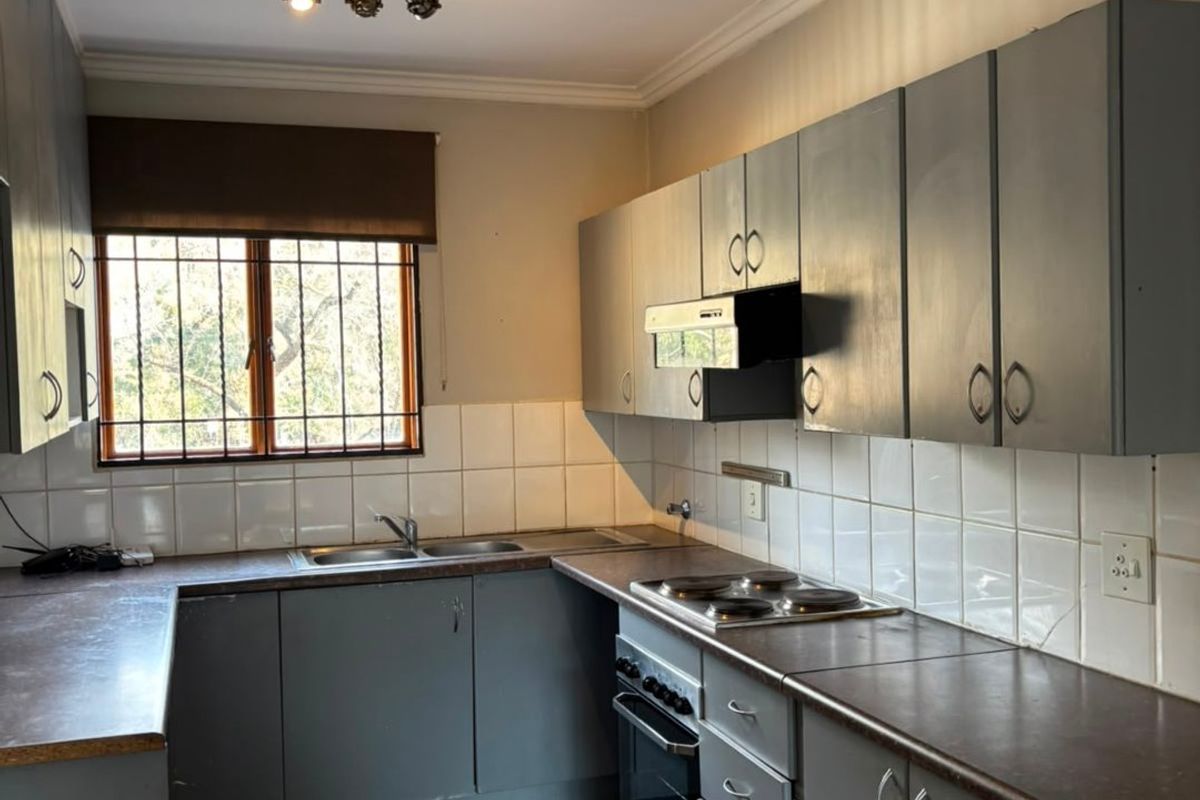 Functional kitchen featuring grey built-in cabinetry, laminate countertops, tiled splashbacks, and integrated electric cooking appliances.