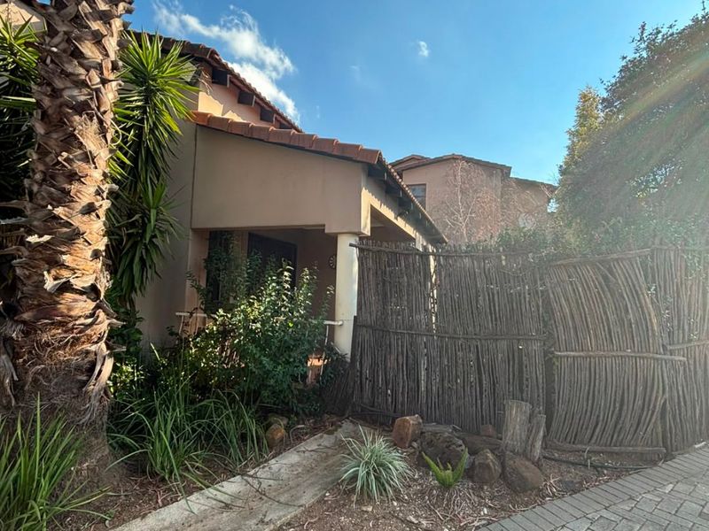 Front exterior view of the house featuring a paved driveway, covered patio area, and established garden landscaping.