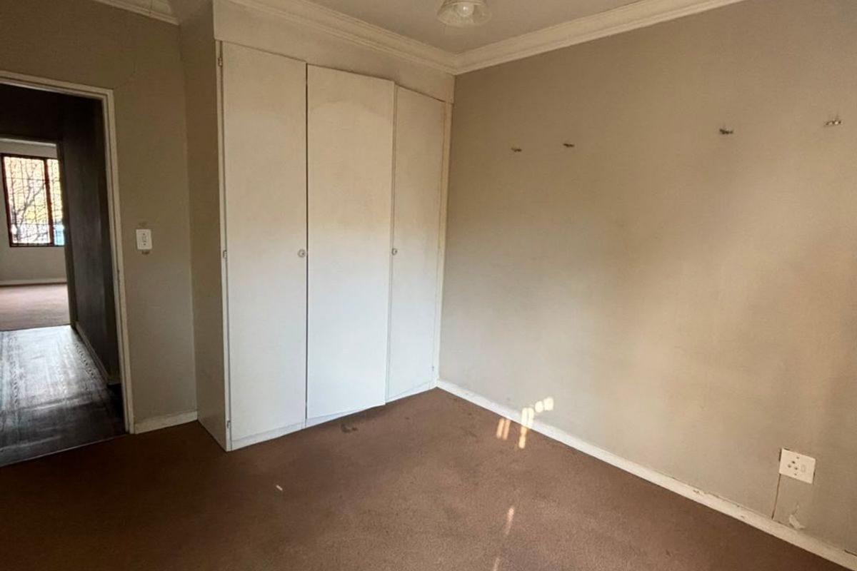 An empty bedroom featuring built-in cupboards, a ceiling fan, and carpeted flooring, requiring cosmetic updates to the walls and flooring.