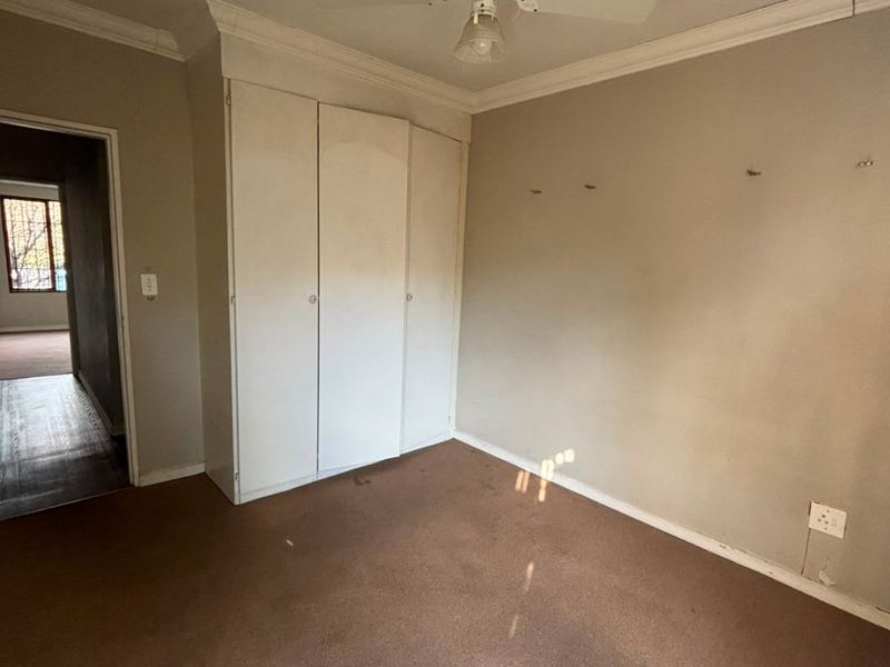 An empty bedroom featuring built-in cupboards, a ceiling fan, and carpeted flooring, requiring cosmetic updates to the walls and flooring.