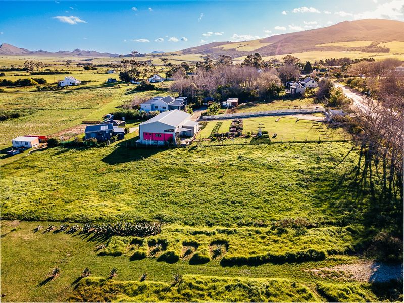 Aerial view of a spacious residential property featuring expansive green grounds, established landscaping, and existing structural buildings in a rural setting.