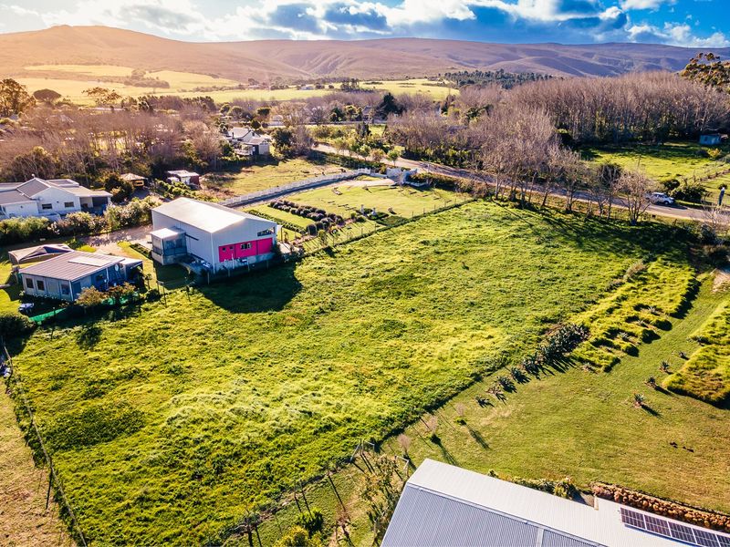 Aerial view of a large residential plot featuring open green space, existing structures with metal roofing, and surrounding rural landscape.