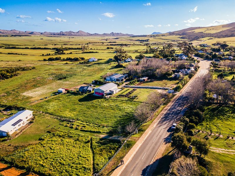 An aerial view of a residential property situated in a rural landscape, featuring surrounding green fields, nearby homes, and direct road access.