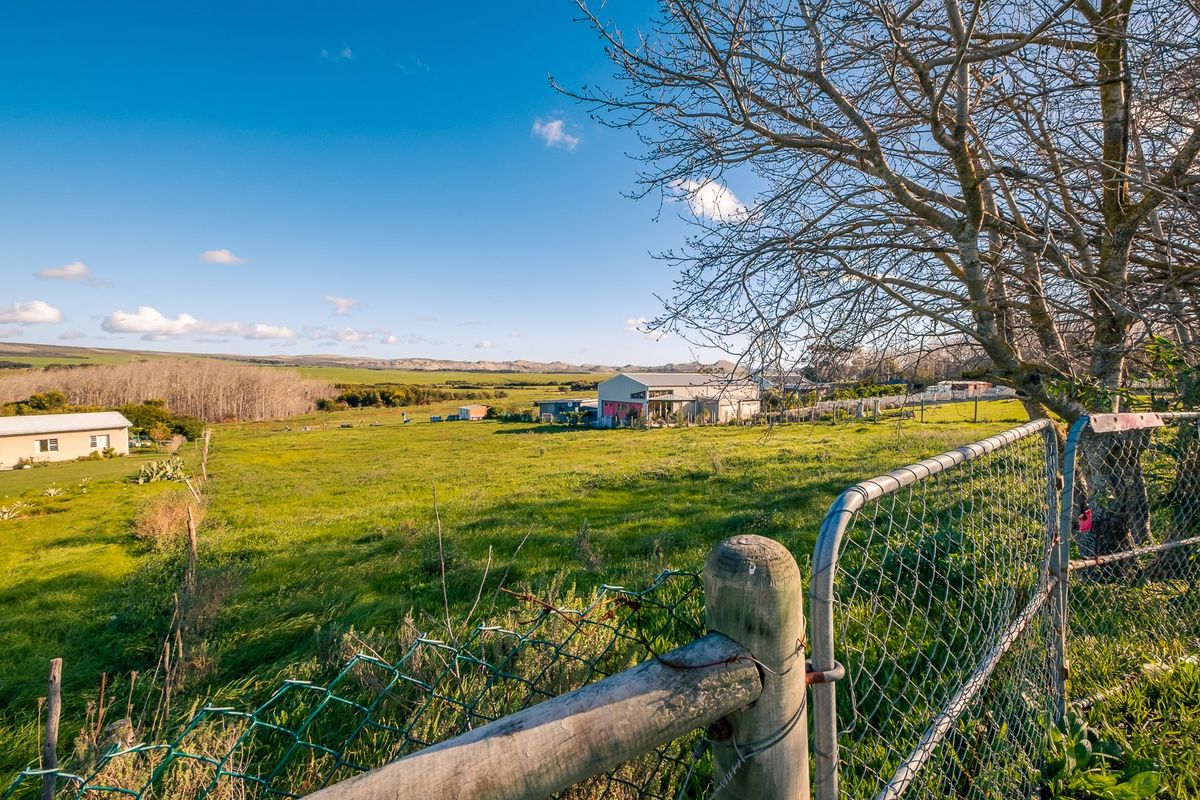 A wide view of a residential vacant land plot featuring open grassland, mature trees, and existing perimeter chain-link fencing.