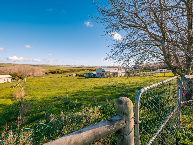 A wide view of a residential vacant land plot featuring open grassland, mature trees, and existing perimeter chain-link fencing.