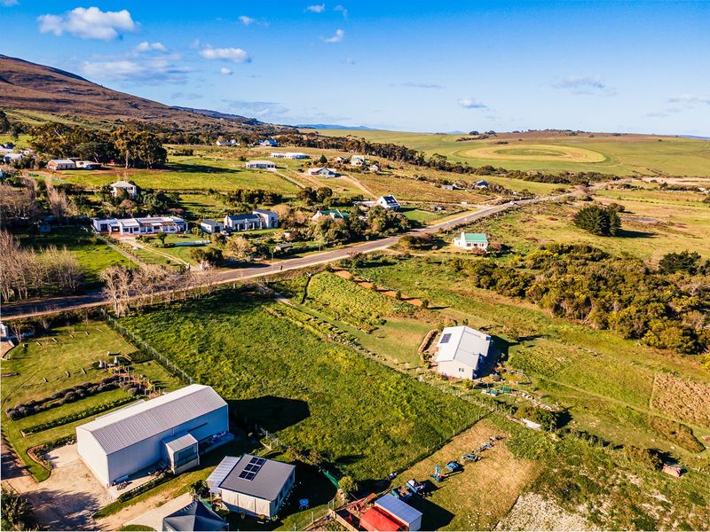 An aerial view of a residential land plot featuring existing structures, solar installations, and surrounding rural landscape with road access.