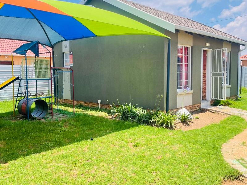 A view of the rear exterior of the house featuring a lawn, paved walkway, and a shade sail structure.