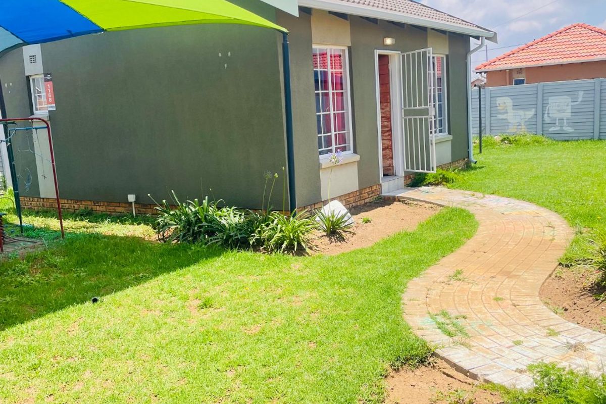 A view of the rear exterior of the house featuring a tiled roof, security gate, paved walkway, and a surrounding garden area.