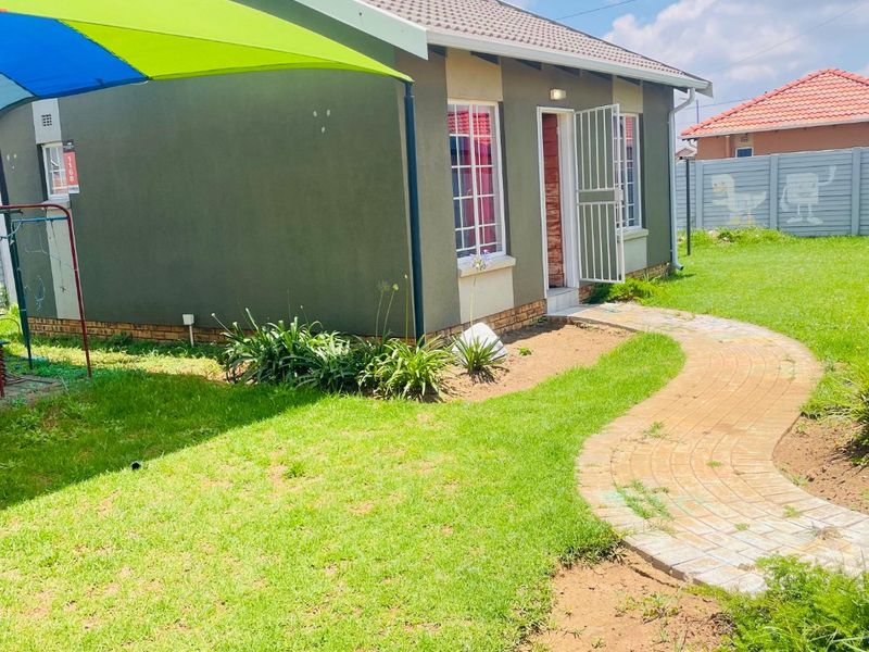 A view of the rear exterior of the house featuring a tiled roof, security gate, paved walkway, and a surrounding garden area.