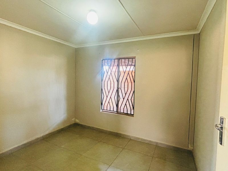 A clean, empty bedroom featuring neutral wall tones, tiled flooring, and a window fitted with a security gate.