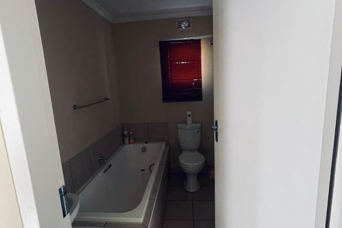 A functional bathroom featuring a built-in bathtub with tiled surround, a standard toilet, and neutral floor tiling.