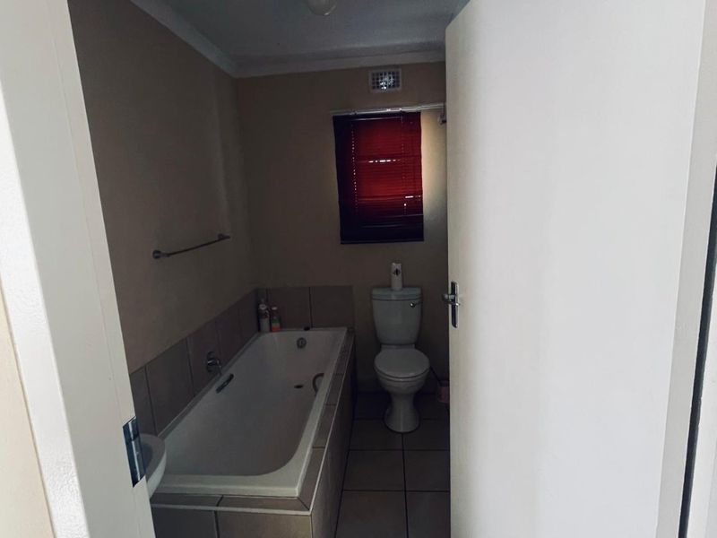 A functional bathroom featuring a built-in bathtub with tiled surround, a standard toilet, and neutral floor tiling.