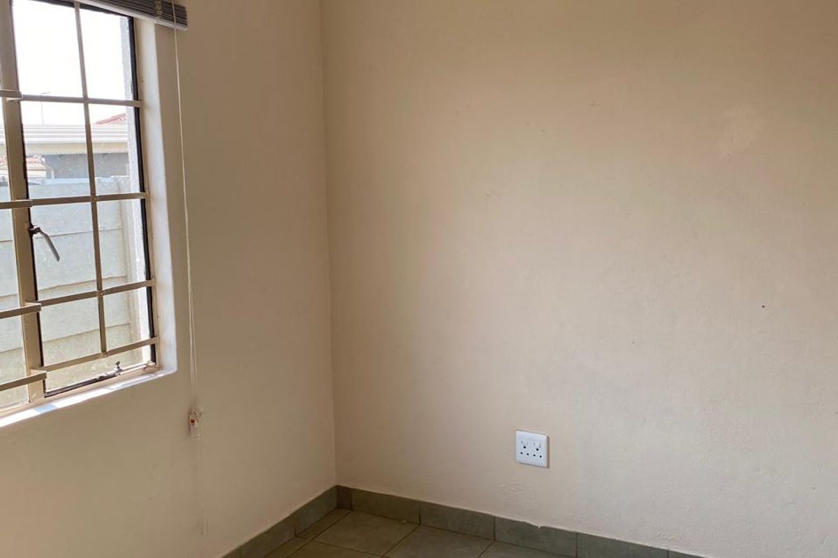 A vacant bedroom featuring tiled flooring, neutral wall paint, and a window fitted with burglar bars and blinds.