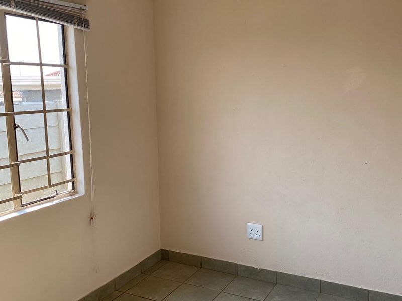 A vacant bedroom featuring tiled flooring, neutral wall paint, and a window fitted with burglar bars and blinds.