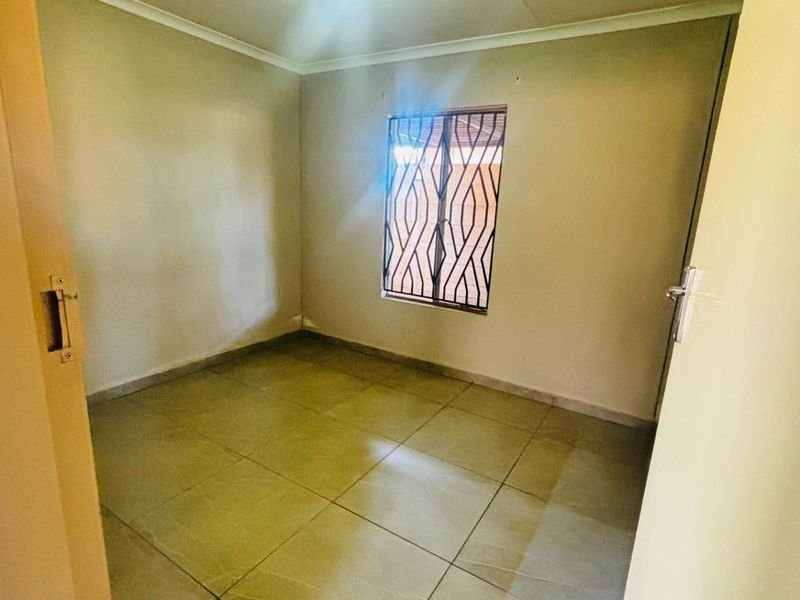 An empty bedroom featuring tiled flooring and security bars on the window, providing a neutral space ready for personalization.