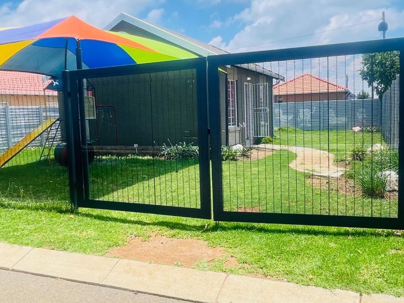 Front view of the property featuring a secure metal mesh gate, a well-maintained lawn, and a paved walkway leading to the entrance.