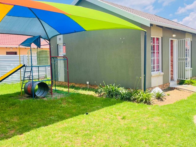 Rear view of the house featuring a lawn, plastered exterior walls, tiled roof, and security features on the windows and door.