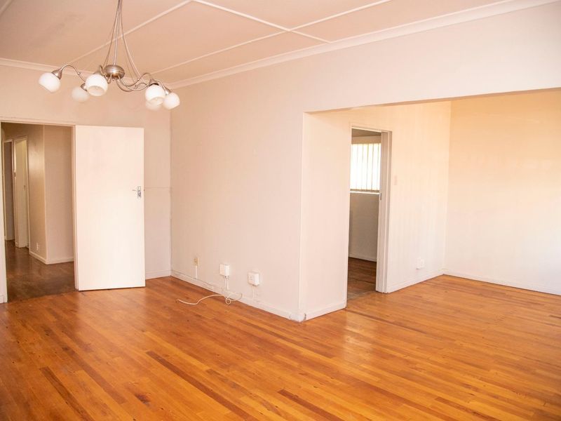 An empty living room featuring polished hardwood flooring, neutral walls, and a central ceiling light fixture, offering a clean and versatile living space.