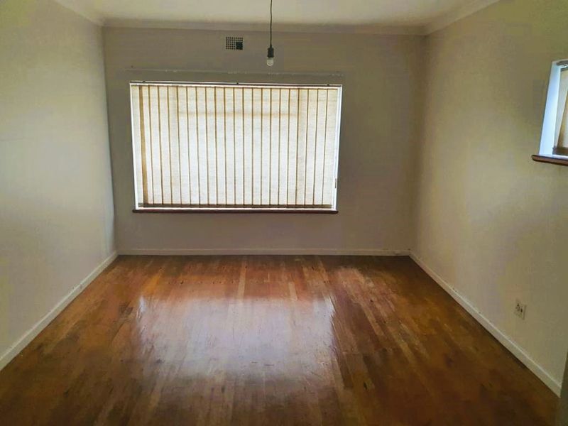 An empty living room featuring polished hardwood flooring, neutral walls, and vertical window blinds, offering a blank canvas for interior design.