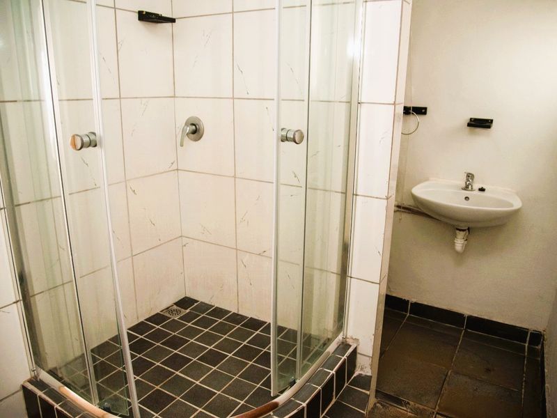 A functional bathroom featuring a glass-enclosed shower and a wall-mounted basin with basic tiled finishes.