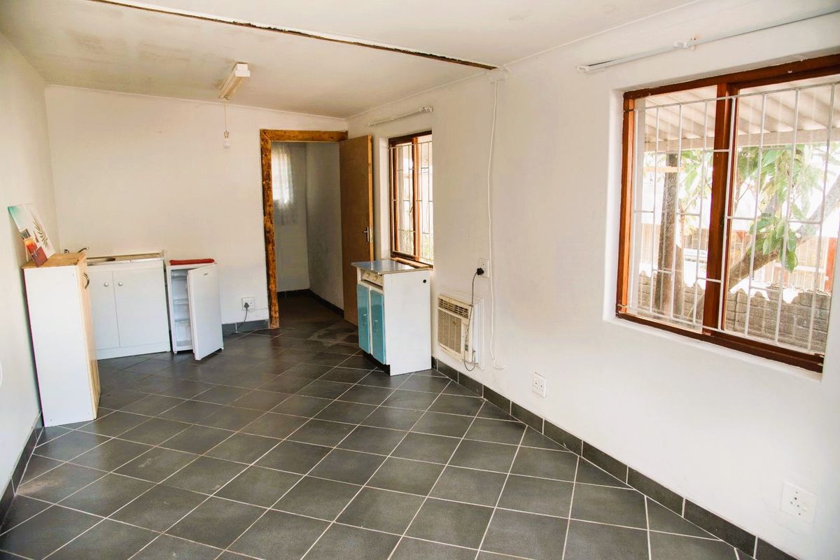 A basic kitchen area featuring tiled flooring, timber-framed windows with security bars, and built-in cabinetry, requiring cosmetic updates to improve its overall condition.