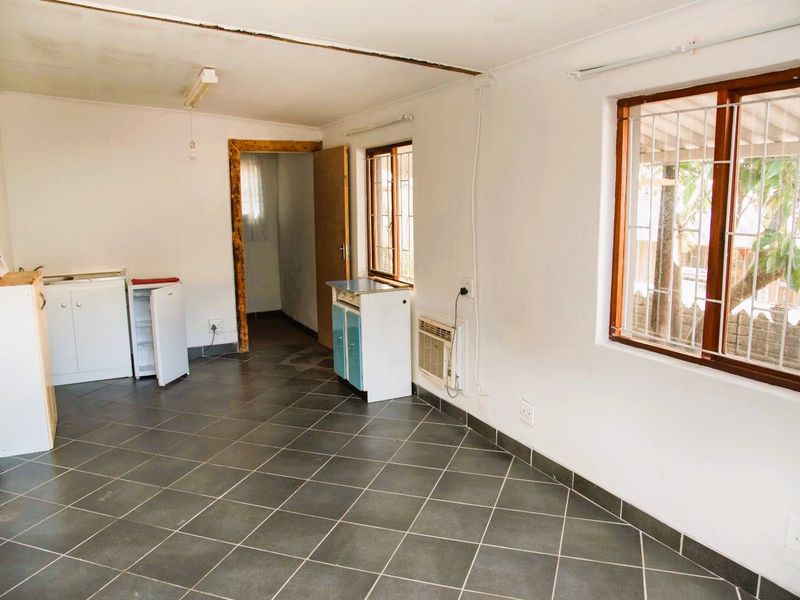 A basic kitchen area featuring tiled flooring, timber-framed windows with security bars, and built-in cabinetry, requiring cosmetic updates to improve its overall condition.
