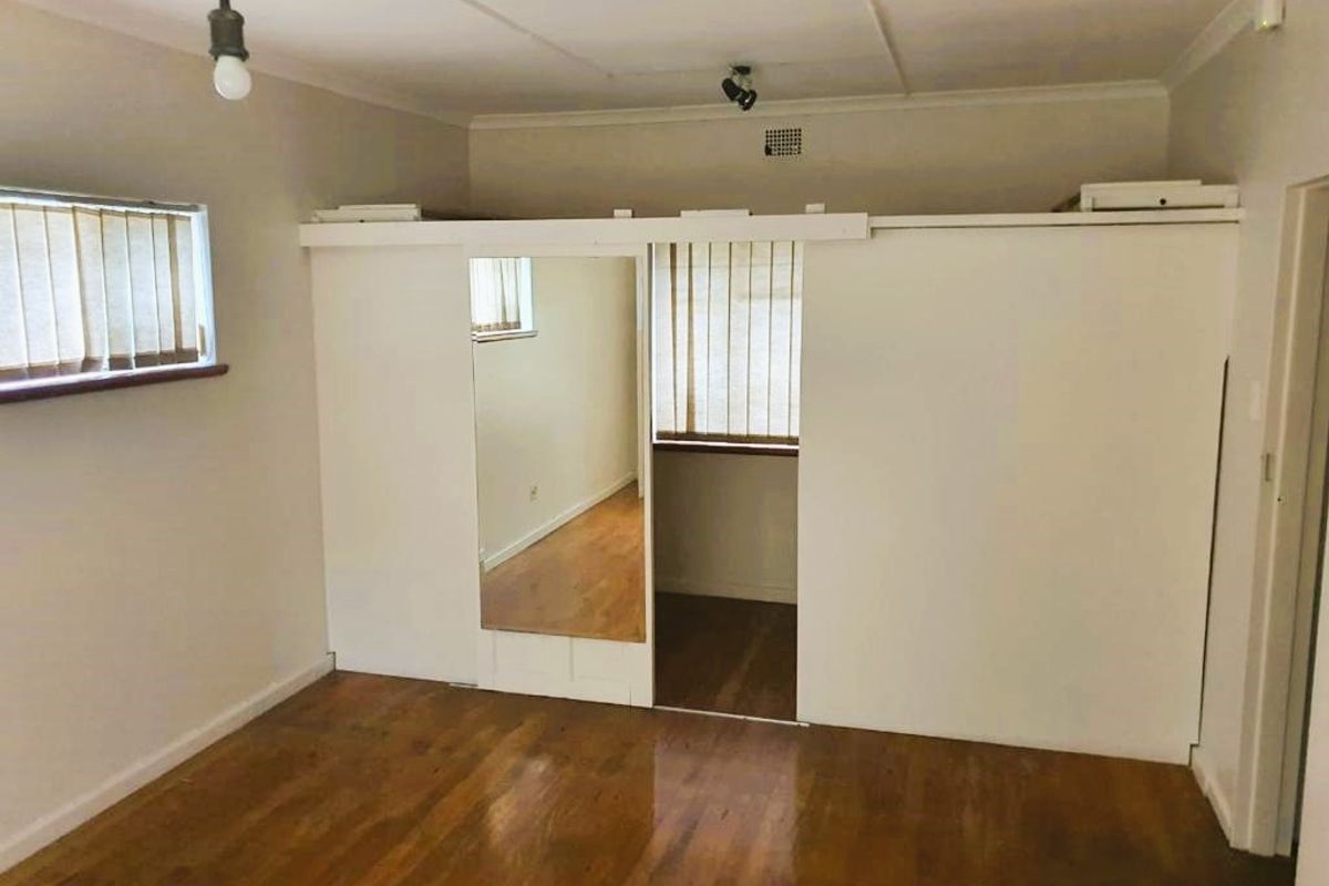 A vacant bedroom featuring hardwood flooring, a built-in wardrobe with a mirrored door, and vertical blinds on the windows.