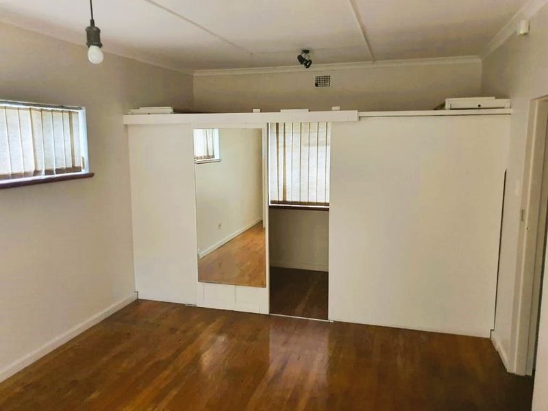 A vacant bedroom featuring hardwood flooring, a built-in wardrobe with a mirrored door, and vertical blinds on the windows.