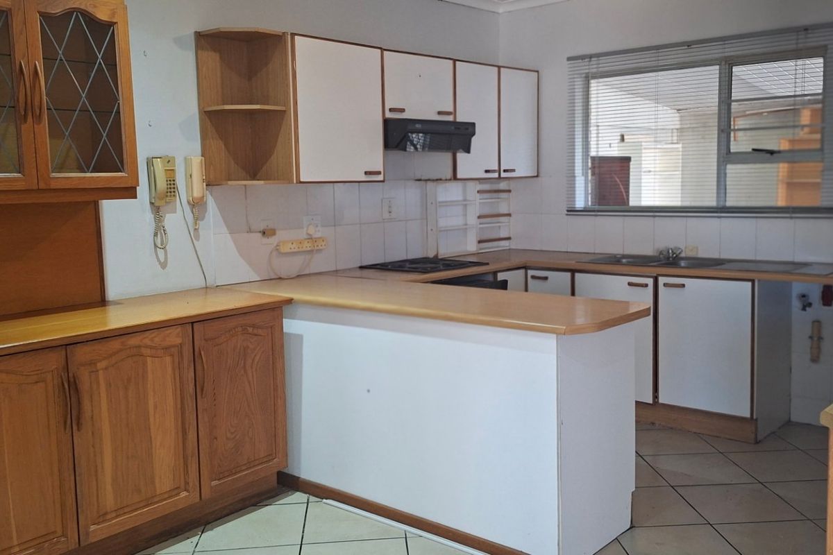 A dated kitchen featuring wooden and white cabinetry, laminate countertops, a gas hob, and tiled flooring, offering potential for a modern renovation.